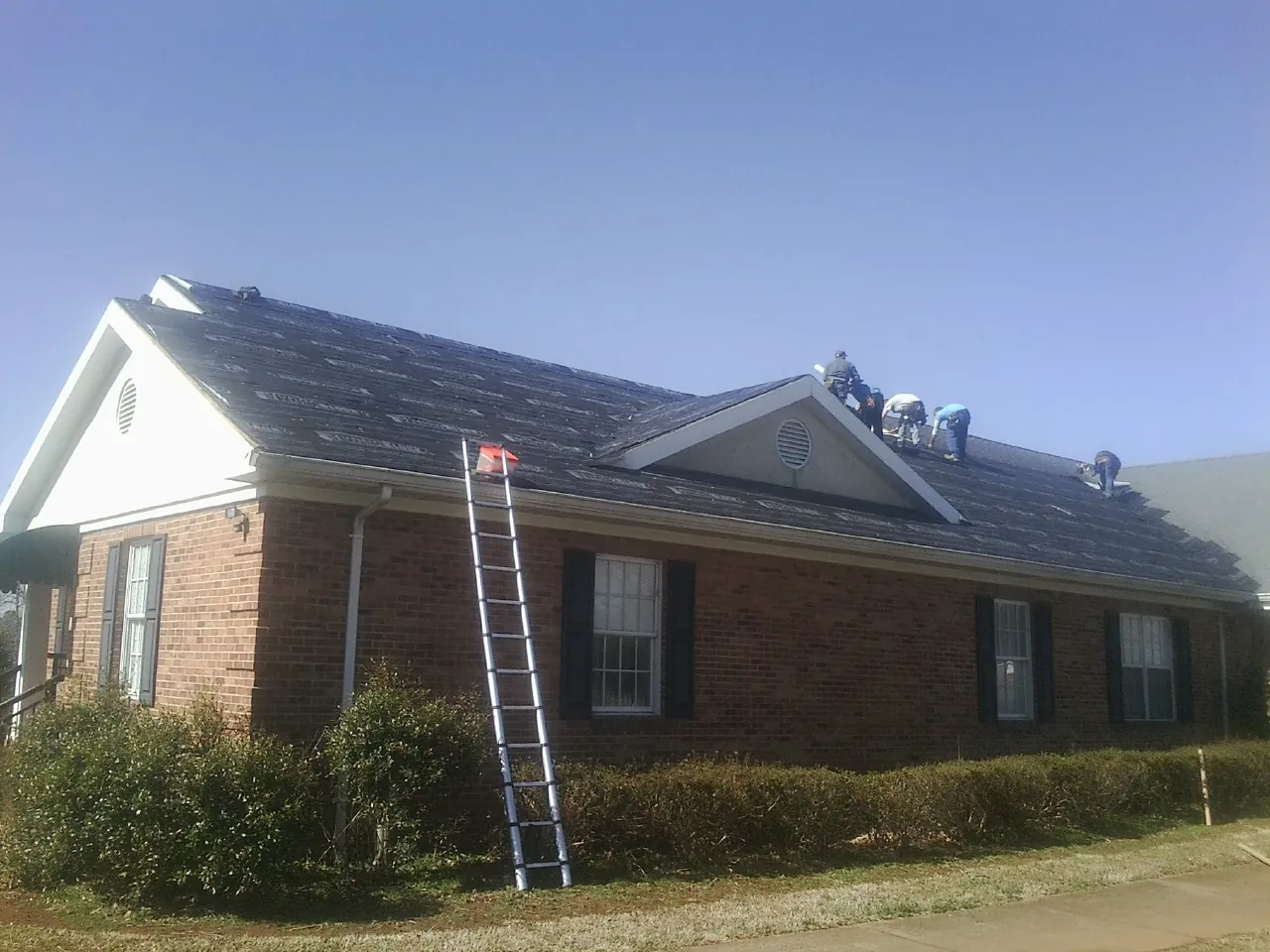 Crew tearing shingles off a brick ranch roof with a ladder set — Metal Roof Repair work by our crew in Naperville
