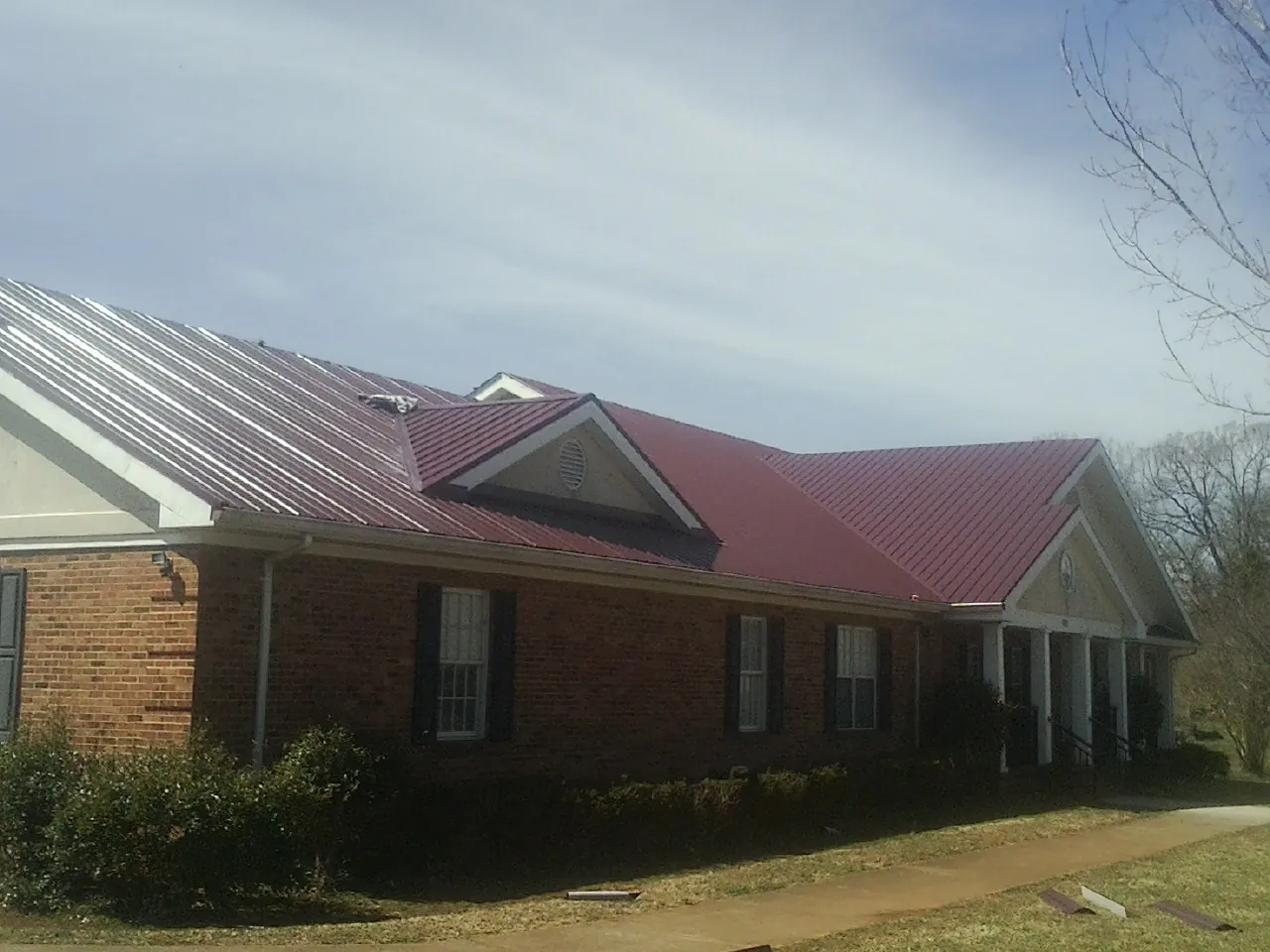 Red metal roof with gabled entries on a long brick building, from a Hail Damage Roof Repair job in Naperville