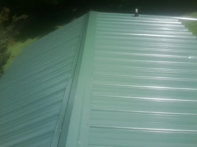 New green metal panels meeting at the ridge of a roof — Flat Roof Repair work by our crew in Naperville