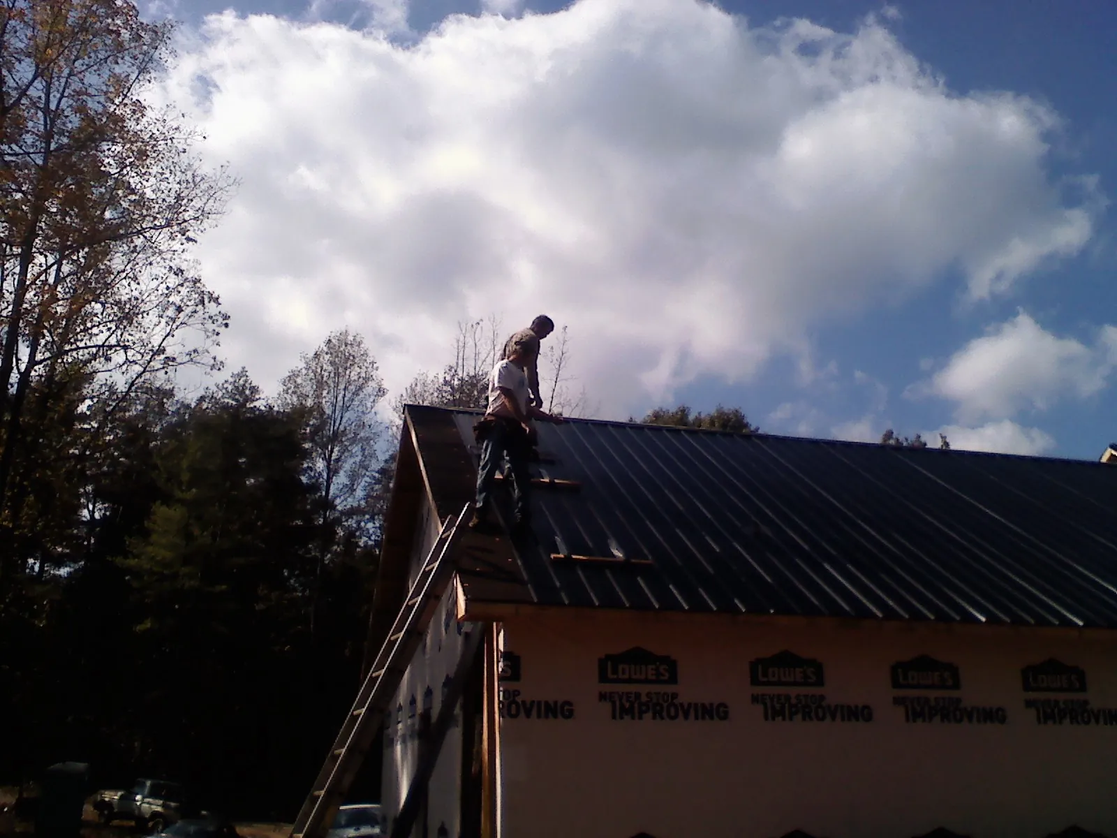 Roofer fastening dark metal panels high against a cloudy sky, from a Roof Inspection job in Naperville