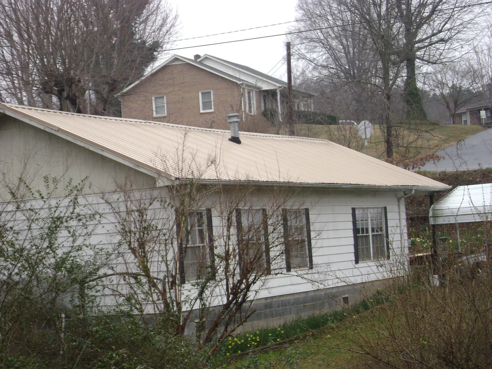 Tan metal roof on a white sided house set into a hillside — Commercial Roofing by Roofing Brothers in Naperville